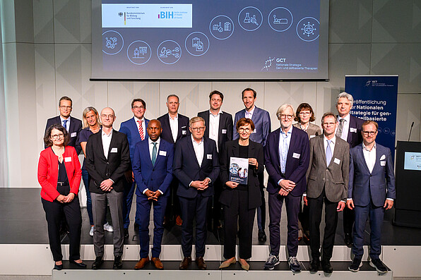 Bundesministerin Bettina Stark-Watzinger erhält von Professor Christopher Baum die Nationale Strategie für gen- und zellbasierte Therapien. Im Hintergrund stehen Mitglieder der Arbeitsgruppe für ein Gruppenfoto.